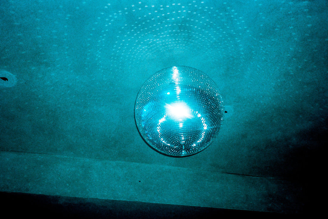 Mirror disco ball suspended from a nightclub ceiling with blue ambient lighting.