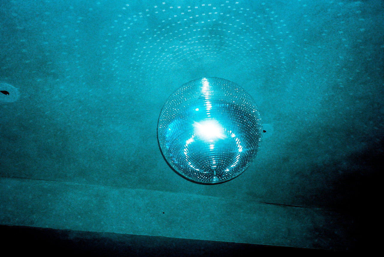 Mirror disco ball suspended from a nightclub ceiling with blue ambient lighting.