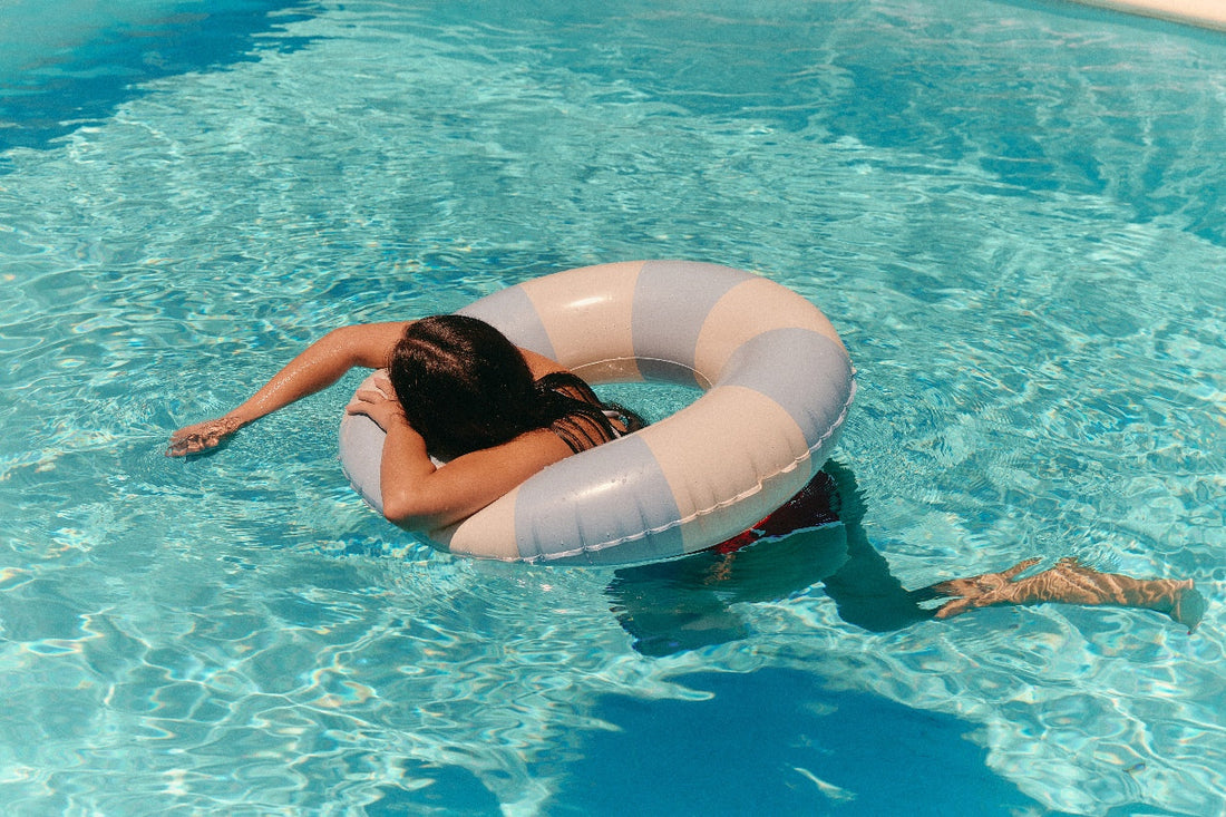Person relaxing on an inflatable pool float in crystal-clear blue water during a sunny summer holiday.